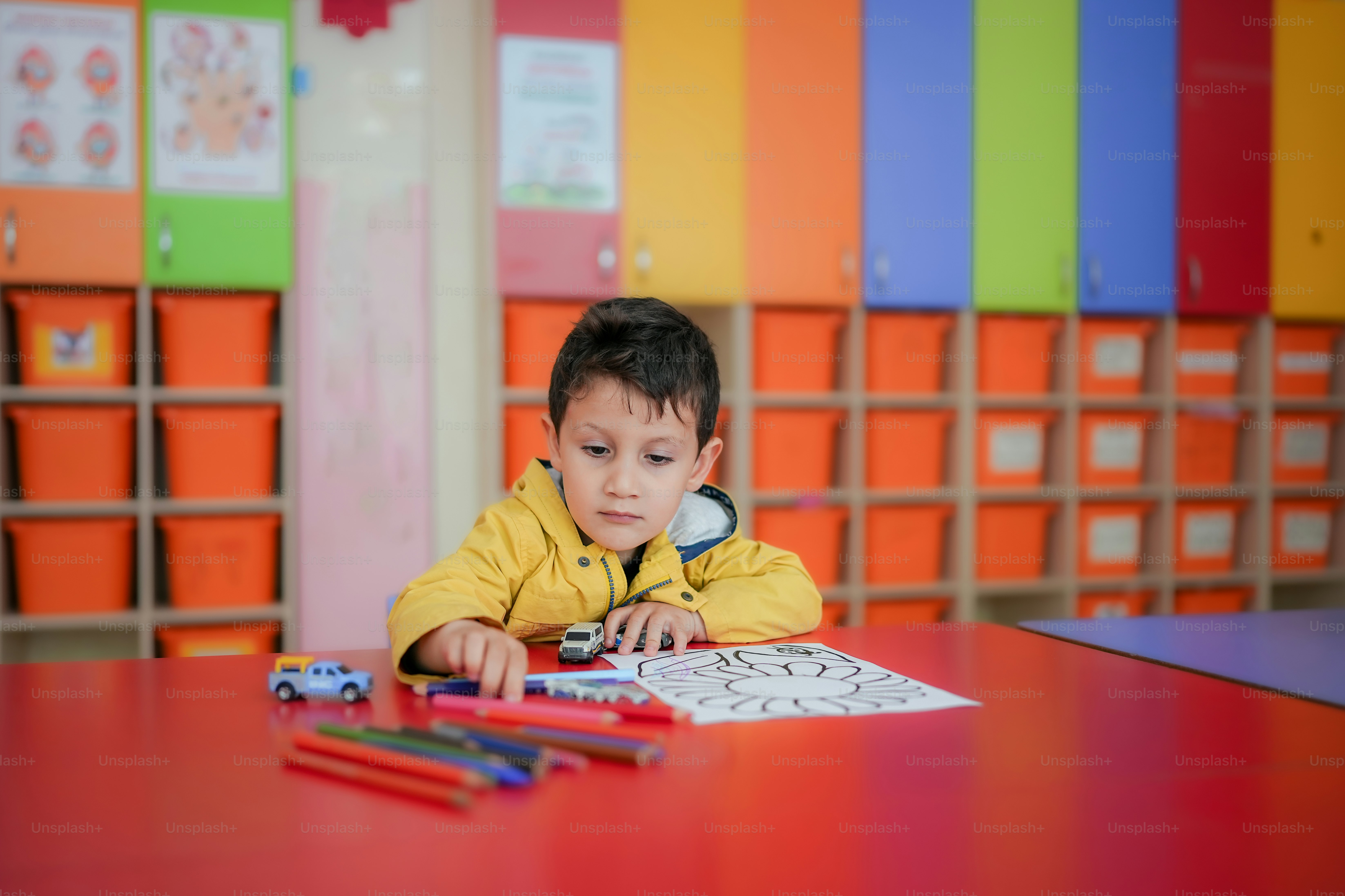 a little boy sitting at a table with some crayons